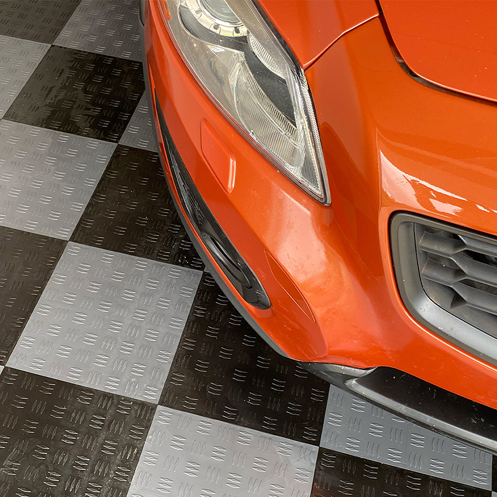 front close up of car sitting on black and gray garage flooring tiles in garage