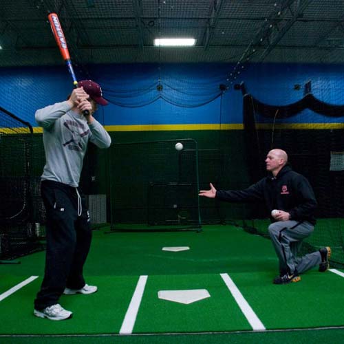 person standing on green home plate mat at indoor batting cage
