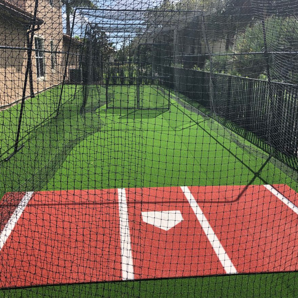clay colored home plate mat in outdoor batting cage with green turf