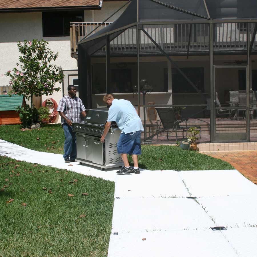 two people moving grill on ground protection mats walkway over grass
