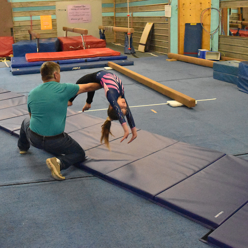 kid tumbling with spotter on gymnastics mats lined up