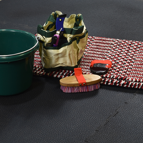 close up of interlocking rubber horse stall mats with horse grooming products and green bucket