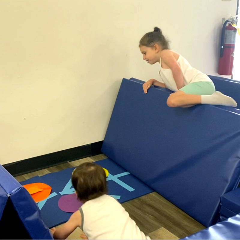 kids climing on a folded gym mat in tumbling class