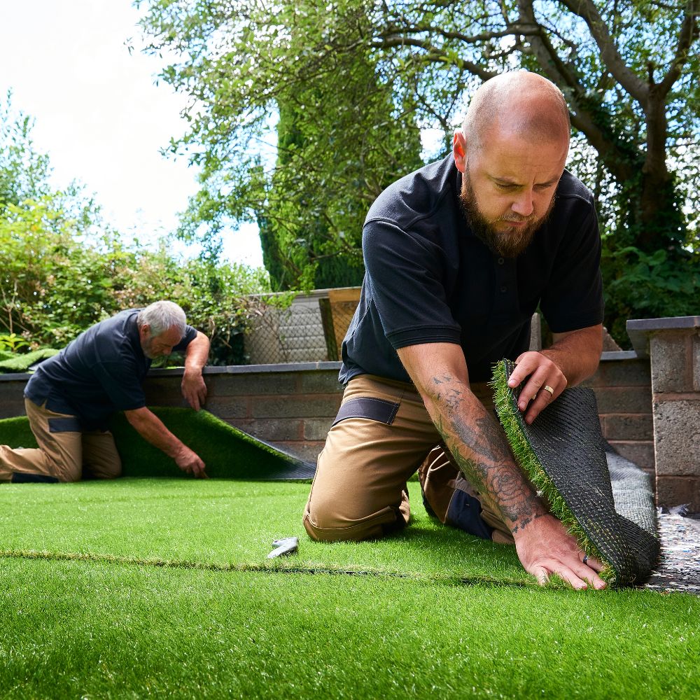 two men installing artificial grass in back yard of home