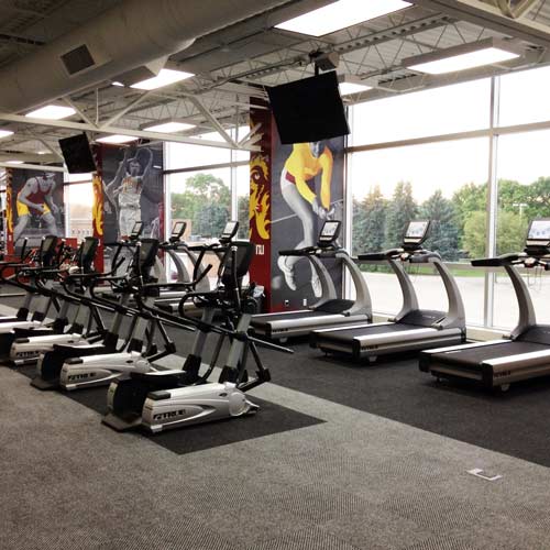 gray and black gym carpet tiles installed at fitness center underneath exercise bikes and treadmills