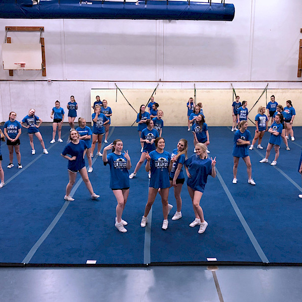cheerleaders standing on blue cheerleading mats in gymnasium