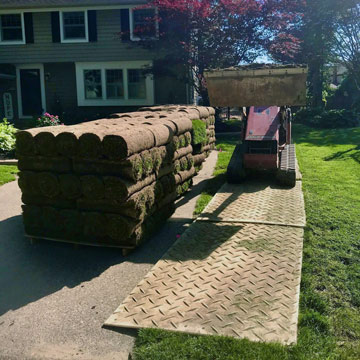 small skid steer driving on ground protection mats over grass