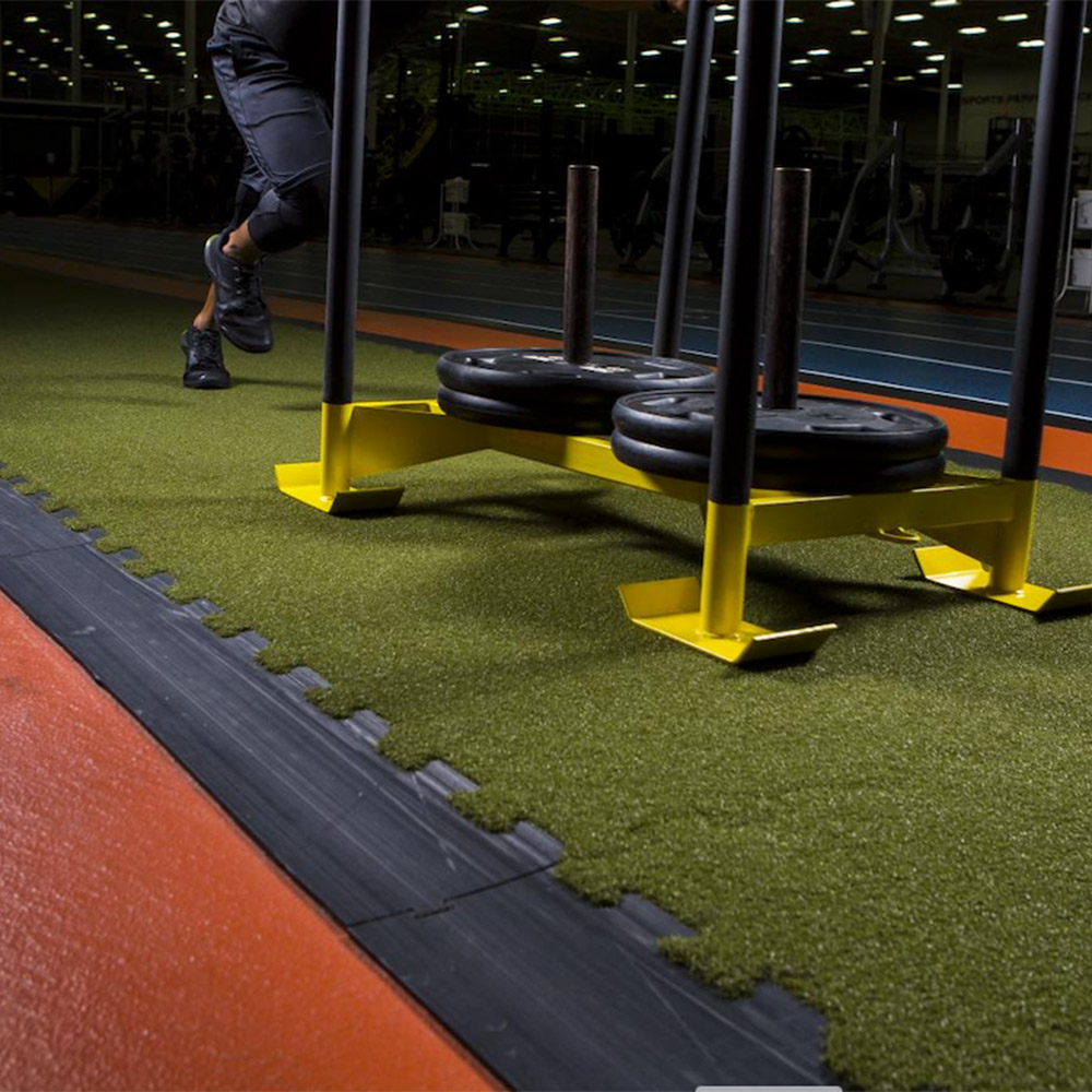 Person pushing weight sled on green turf tiles