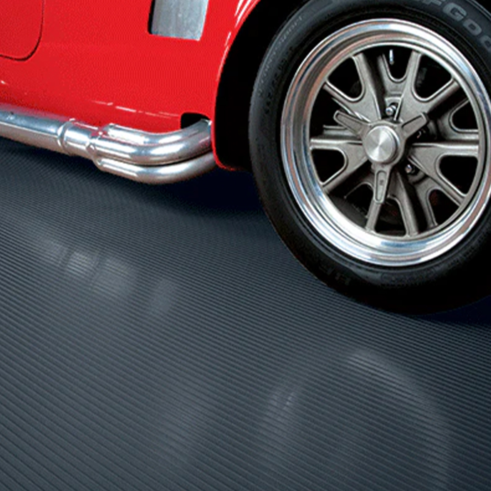 Red care with sidepipes parked on G-Floor Ribbed Tread Garage Floor Roll 55 Mil x 8.6x24 Ft. in midnight black
