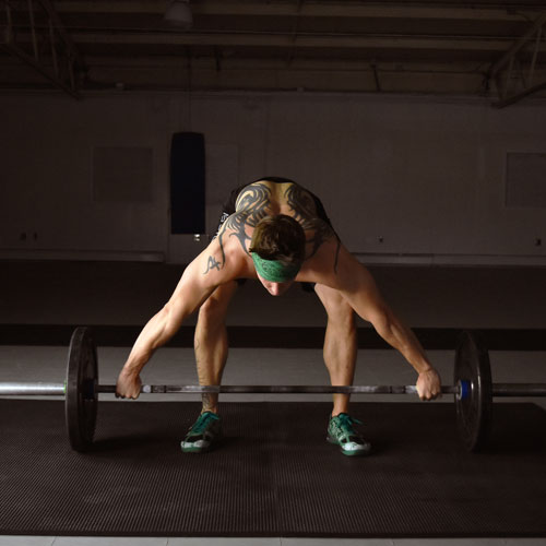 man lifting weights on horse stall mats in a gym