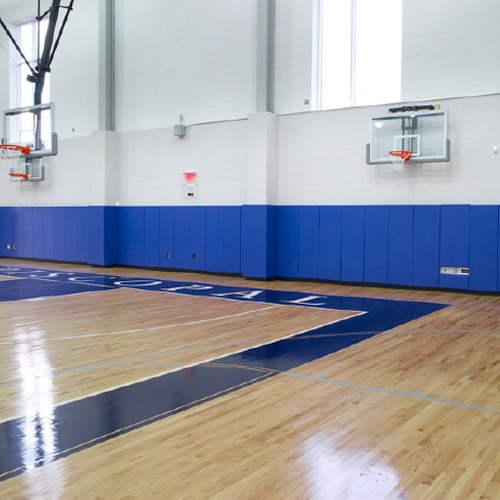 large gym with basketball hoops and wall pads on the walls