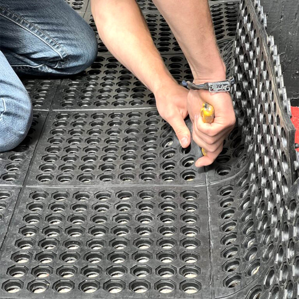 person cutting wash rack horse stall mats with sharp utility knife