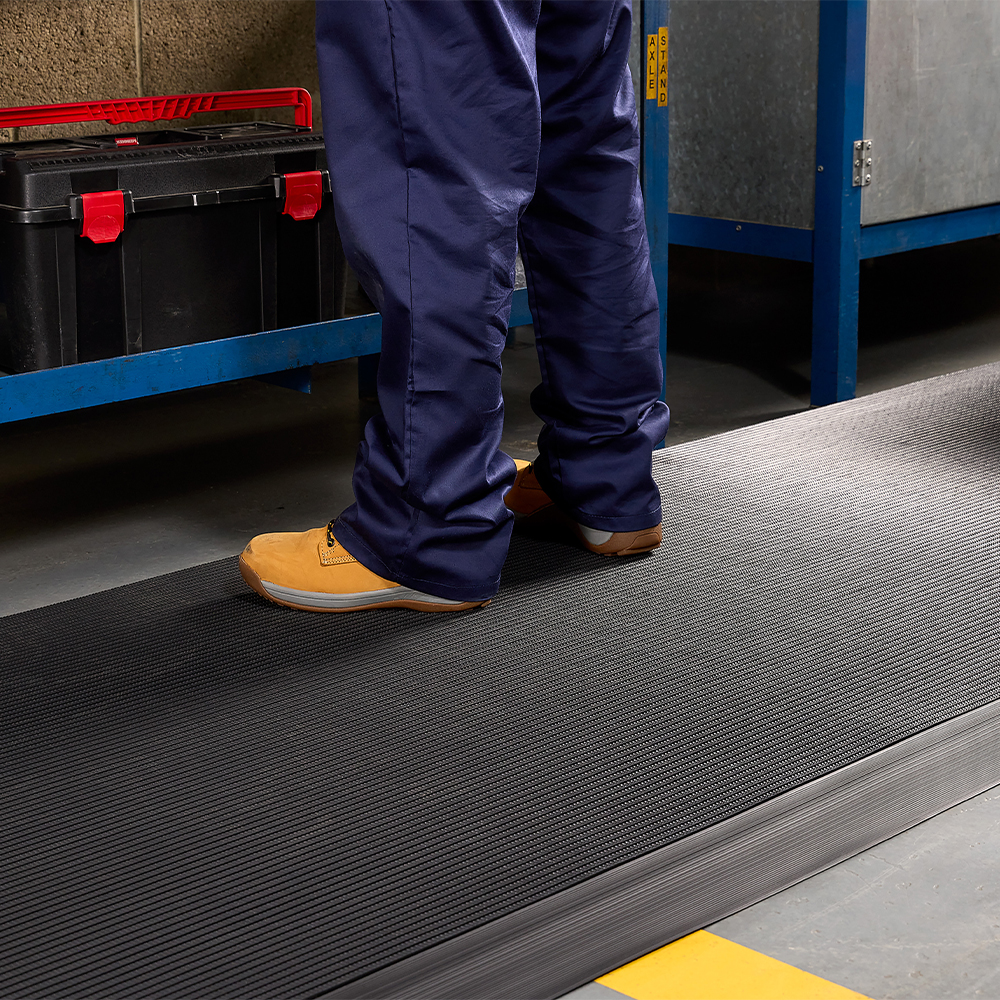 person with work boots standing on black firmagrip matting at workbench