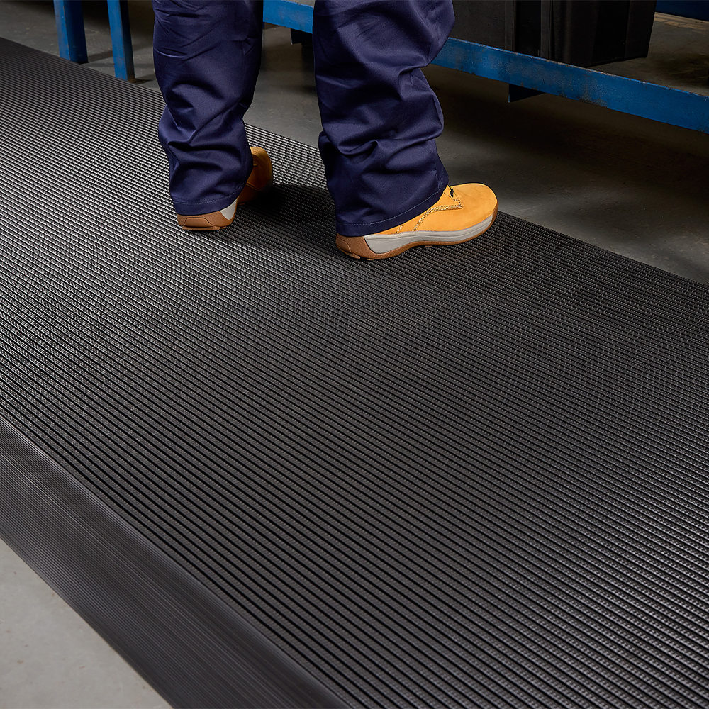 close up of person standing at industrial workbench on Firmagrip Matting