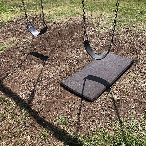brown rubber swing set mat on dirt underneath swing sets at park