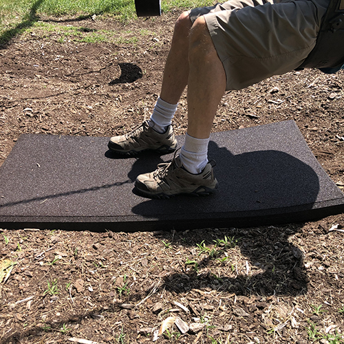 brown playground mat over wood mulch under swing with person sitting in swing