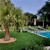 artificial turf lawn near in ground pool with palm trees in lawn and patio chairs and concrete pavers